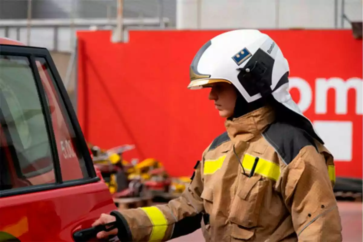 Bombera con uniforme y casco abriendo la puerta de un vehículo rojo.