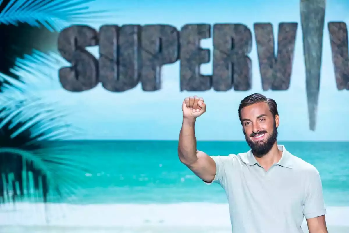 Borja González con barba y camiseta clara sonríe y levanta el puño frente a un fondo de playa y el logo de Supervivientes Borja González con barba y camiseta clara sonríe y levanta el puño frente a un fondo de playa y el logo de Supervivientes