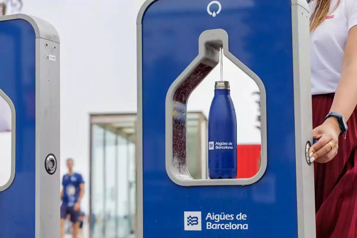 Persona llenando una botella azul reutilizable en una fuente pública de agua en Barcelona.