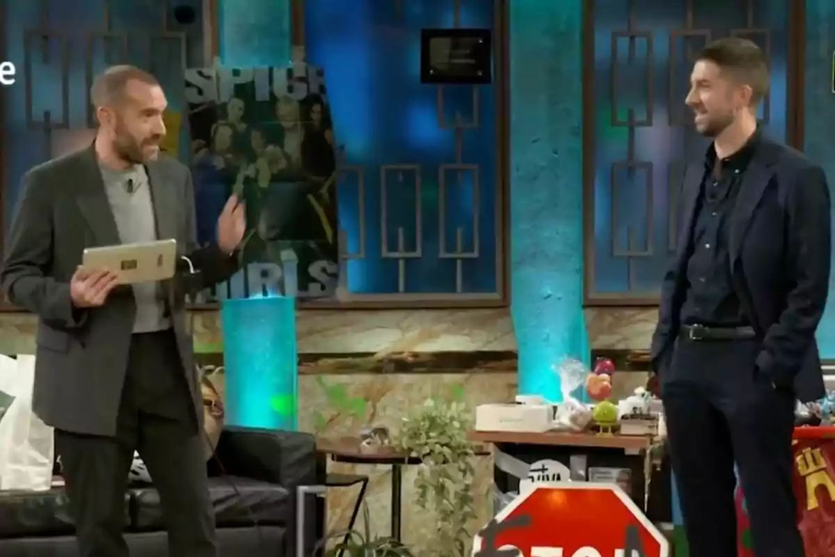 Jorge Ponce y David Broncano conversan en un set de televisión decorado con carteles y objetos variados, una de ellas sostiene una tablet mientras la otra sonríe. Jorge Ponce y David Broncano conversan en un set de televisión decorado con carteles y objetos variados, una de ellas sostiene una tablet mientras la otra sonríe.