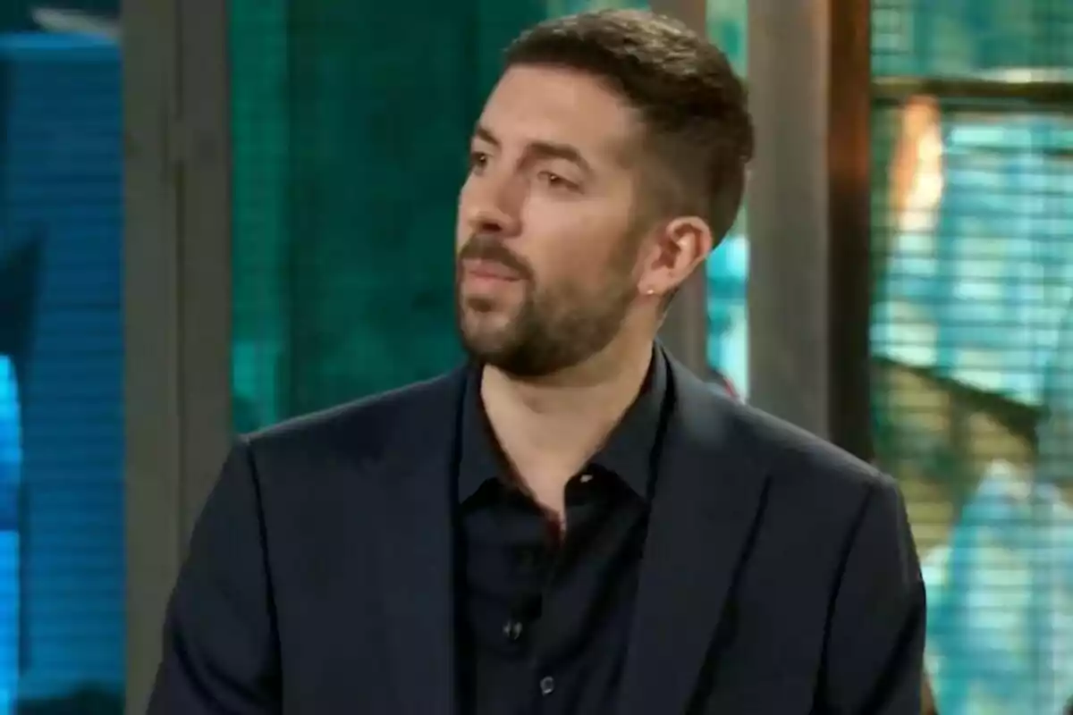 David Broncano con barba corta y cabello oscuro vestido con saco negro en un ambiente interior con fondo desenfocado en 'La Revuelta'.