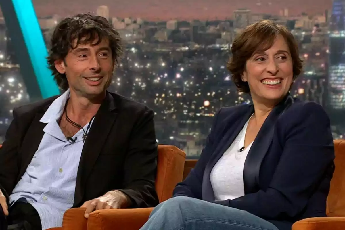 Bruno Oro y Clara Segura sentadas en un sofá durante una entrevista en un programa de televisión, Col·lapse, con una ciudad iluminada de fondo. Bruno Oro y Clara Segura sentadas en un sofá durante una entrevista en un programa de televisión, Col·lapse, con una ciudad iluminada de fondo.