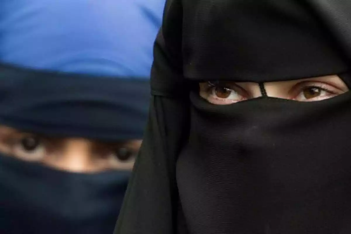 Dos personas con niqab, una en primer plano con un niqab negro y otra al fondo con un niqab azul.