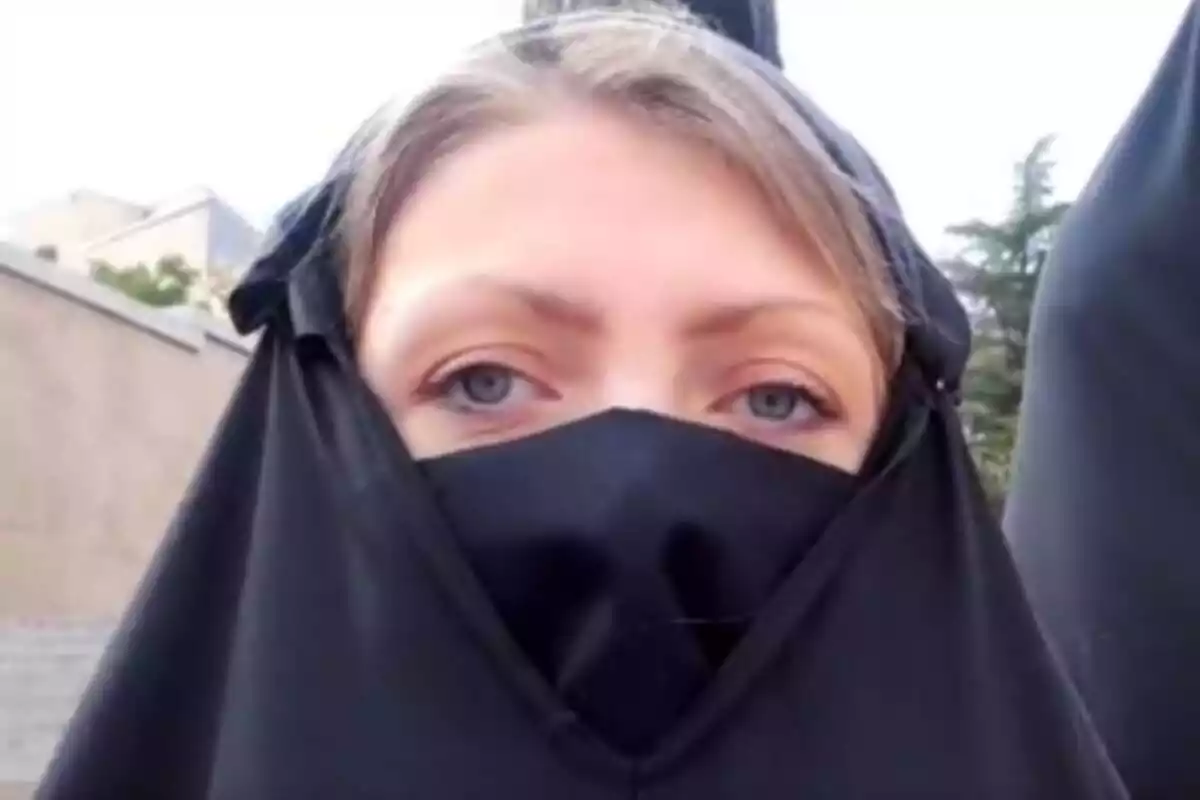 Primer plano de una mujer rubia con ojos azules llevando un burka que le cubre casi todo el rostro menos los ojos y la frente