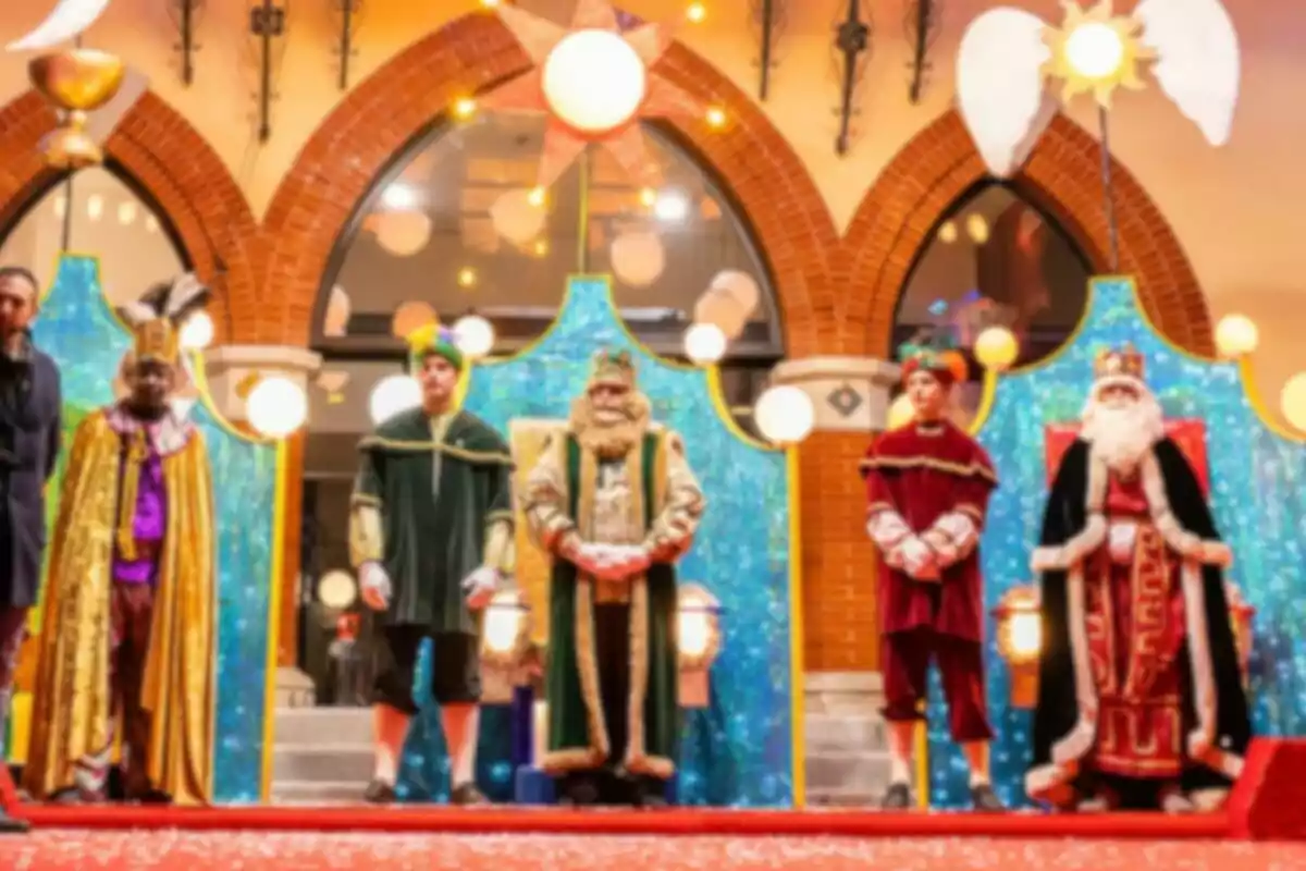 Un grupo de personas disfrazadas de los Reyes Magos y sus ayudantes posan en un escenario decorado con luces y fondos brillantes.