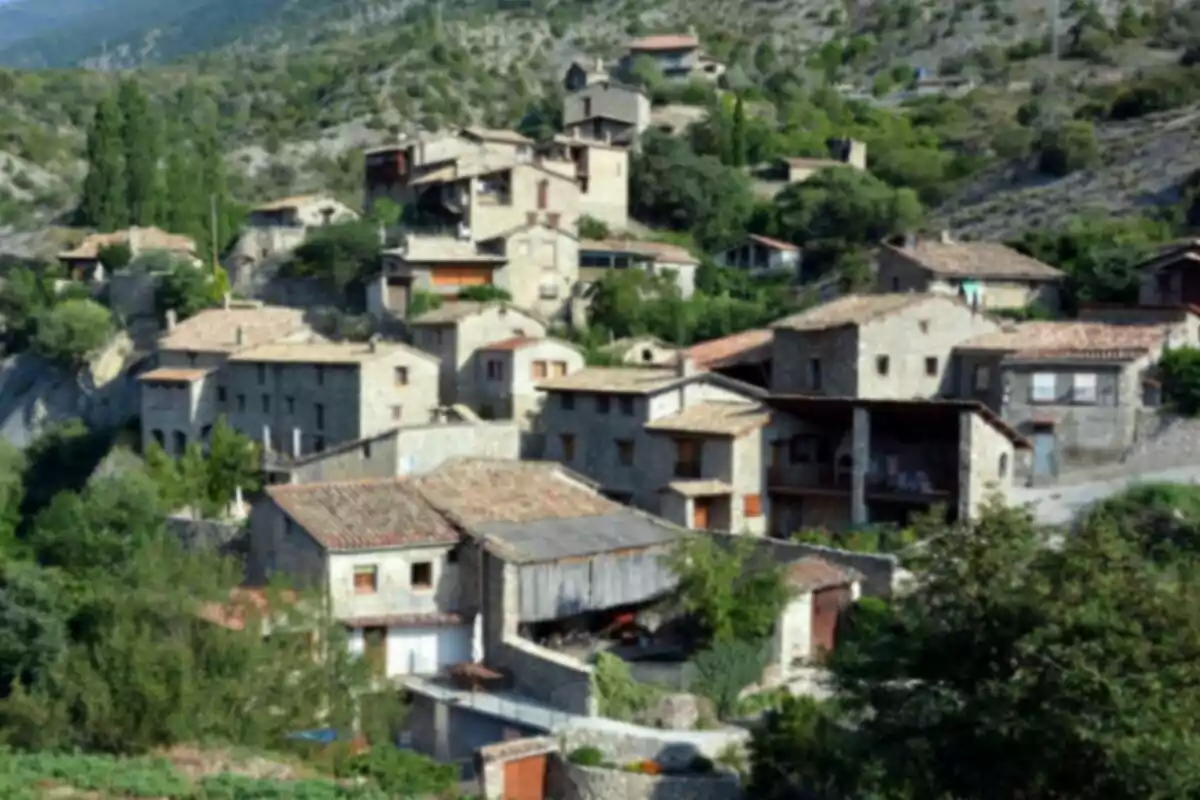Vista de un pintoresco pueblo de montaña con casas de piedra y tejados de tejas rodeado de vegetación y colinas. Vista de un pintoresco pueblo de montaña con casas de piedra y tejados de tejas rodeado de vegetación y colinas.