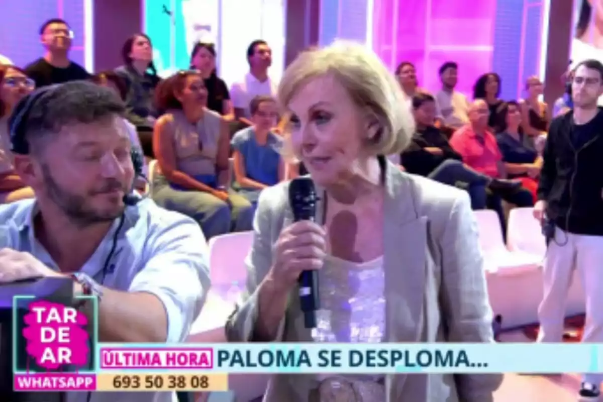 Paloma Barrientos mayor sostiene un micrófono y habla en Tardear en vivo, mientras un hombre con auriculares la observa y el público está sentado al fondo. Paloma Barrientos mayor sostiene un micrófono y habla en Tardear en vivo, mientras un hombre con auriculares la observa y el público está sentado al fondo.