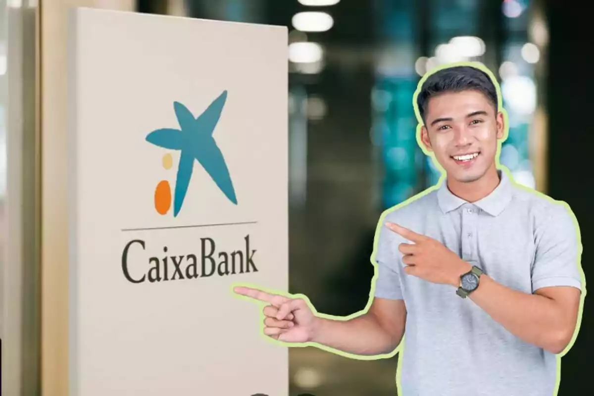 Un hombre sonriente con una camisa gris señala un cartel de CaixaBank.