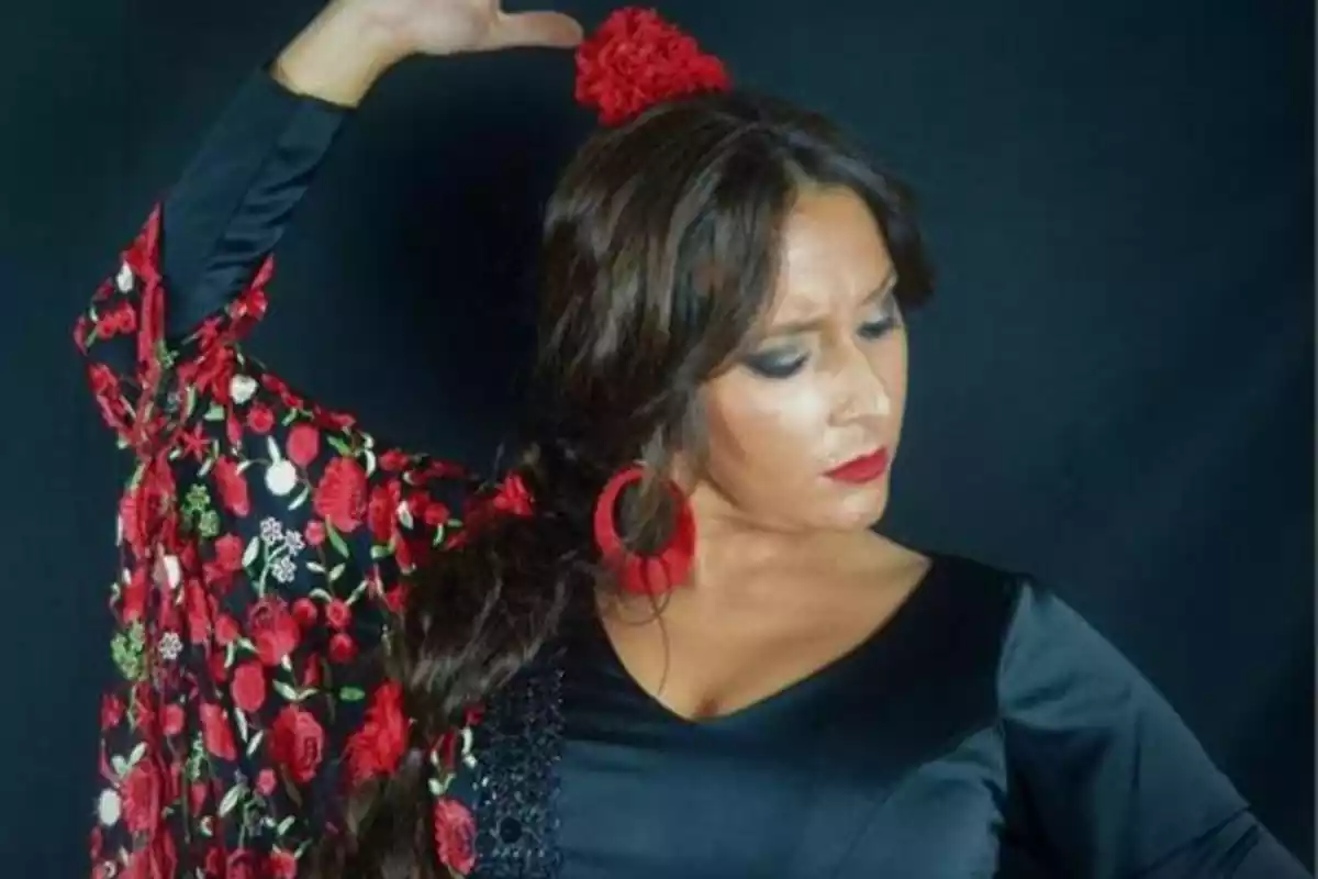 Una mujer con un vestido negro y rojo de flamenco con un pompón en la cabeza y unos pendientes de color rojos