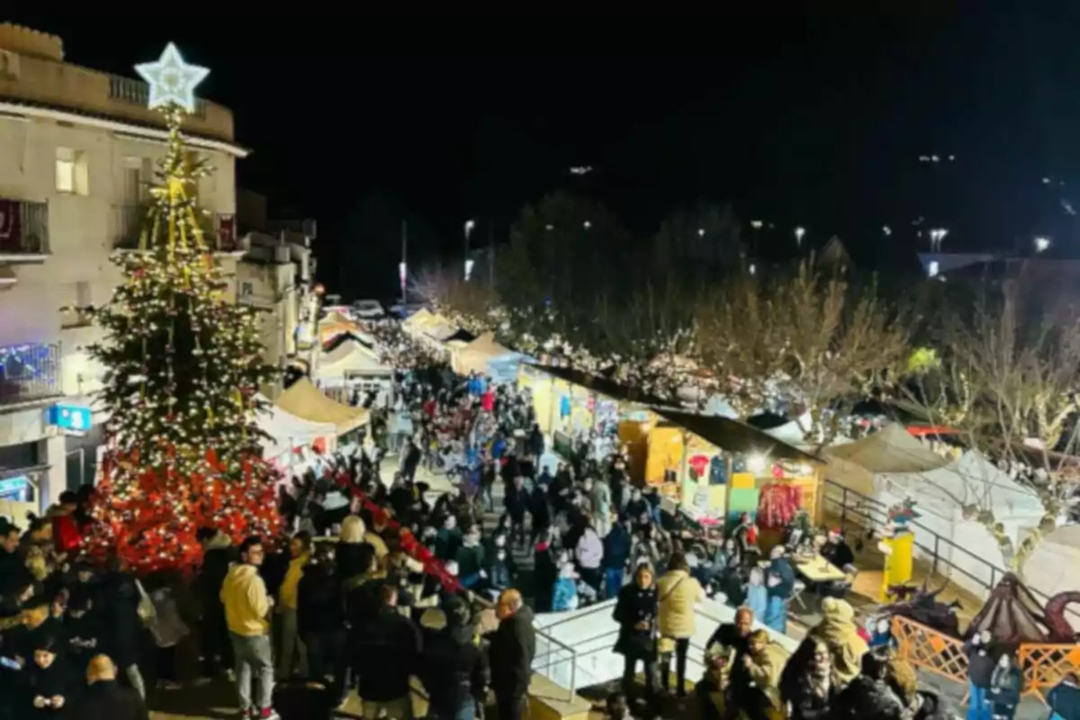 Una concurrida feria navideña nocturna con un gran árbol de Navidad iluminado y puestos decorados.