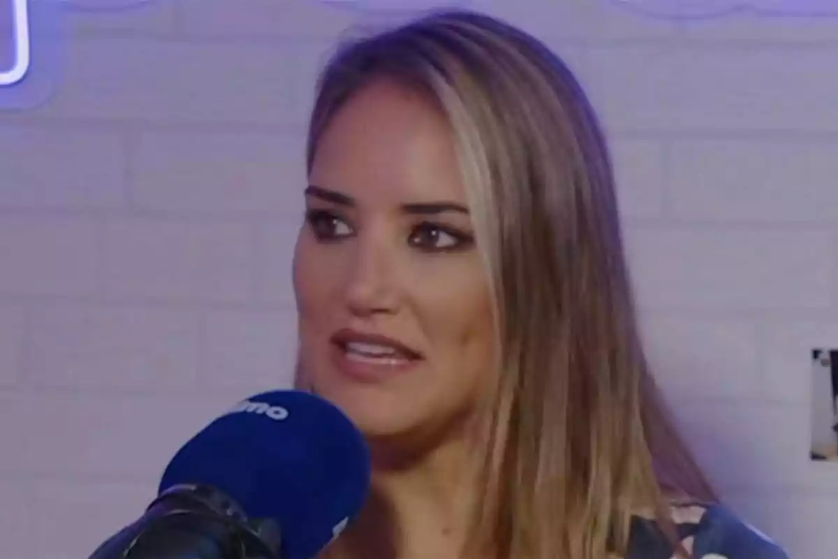 Mujer rubia hablando frente a un micrófono azul en un estudio de grabación.