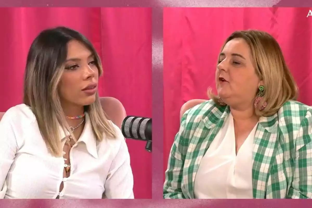 Dos mujeres conversando frente a micrófonos con un fondo de cortinas rosas.