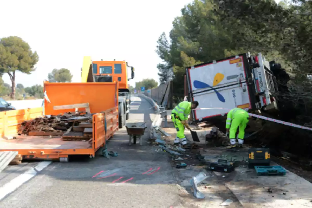 Imagen del punto de la AP-7, en el Vendrell (Tarragona), en la que aparece un camión volcado fuera de la vía y dos personas haciendo su trabajo el día posterior al accidente
