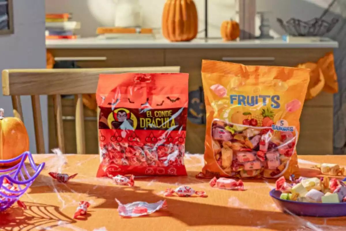 En la imagen se observan dos bolsas de dulces sobre una mesa decorada con temática de Halloween, una bolsa roja con la imagen de un vampiro y el texto En la imagen se observan dos bolsas de dulces sobre una mesa decorada con temática de Halloween, una bolsa roja con la imagen de un vampiro y el texto
