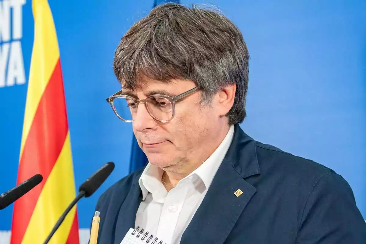 Carles Puigdemont en una conferencia con una bandera catalana de fondo.