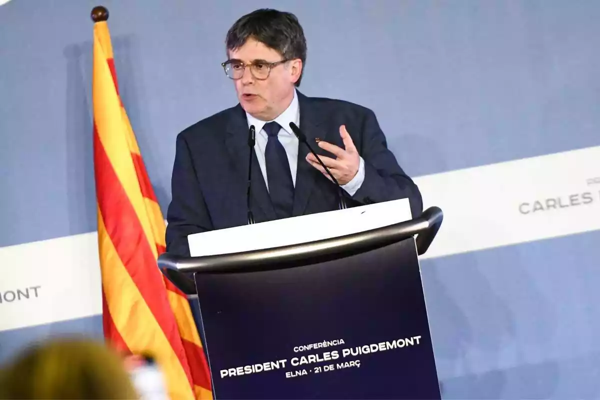 Carles Puigdemont hablando desde un atril de color azul con una bandera catalana de fondo
