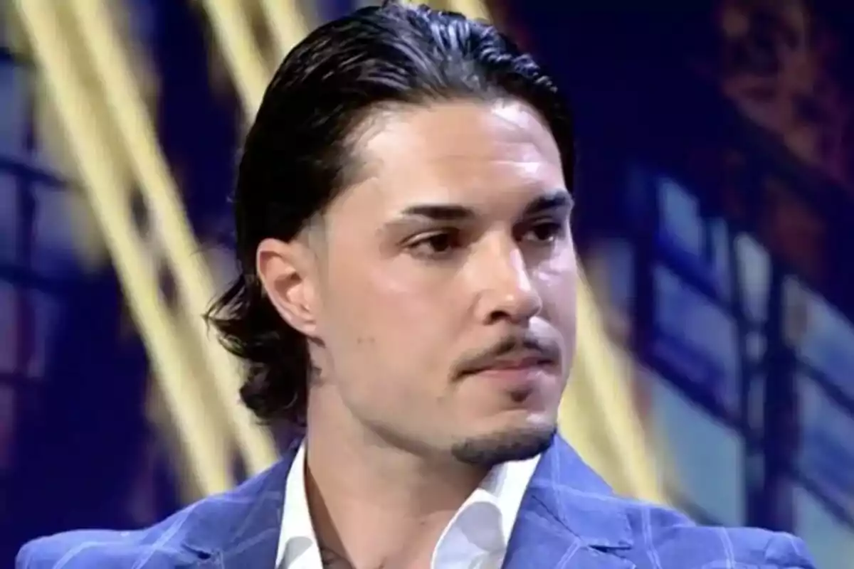 Carlo Costanzia con cabello oscuro y peinado hacia atrás, vistiendo un traje azul, en un entorno de estudio de televisión en De Viernes.