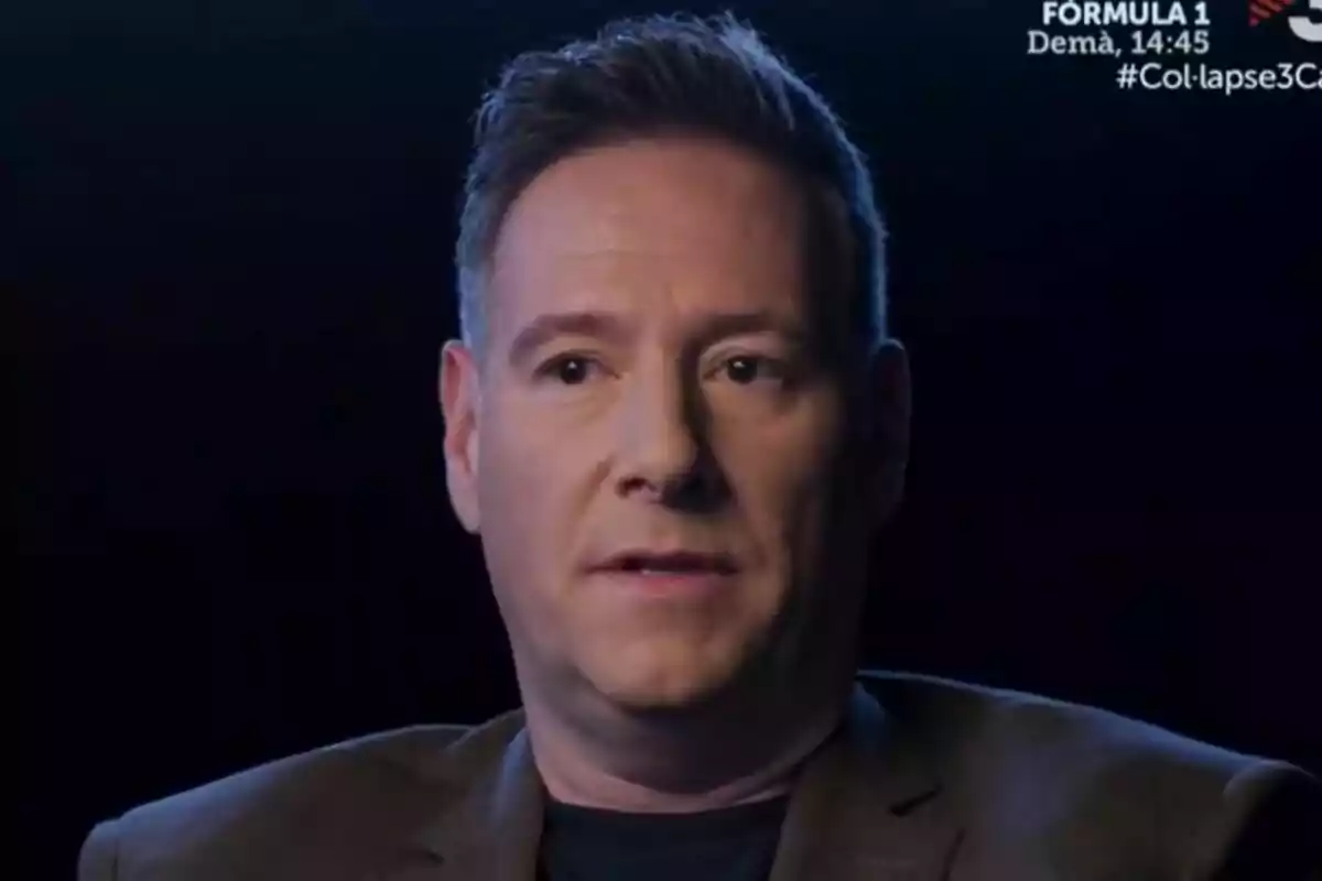 Carlos Latre de cabello corto y expresión seria sentado frente a un fondo oscuro en Col·lapse