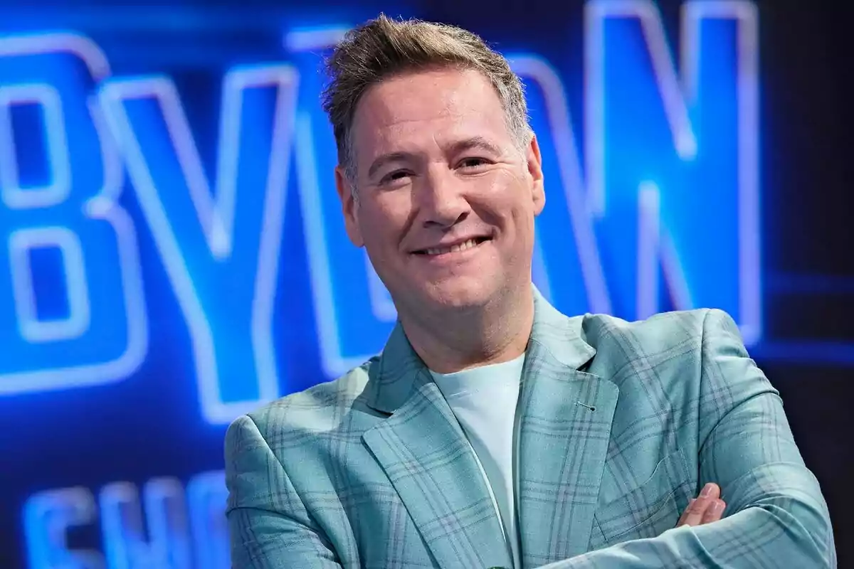 Fotografía de Carlos Latre sonriendo con un fondo azul y letras borrosas en la presentación de Babylon Show