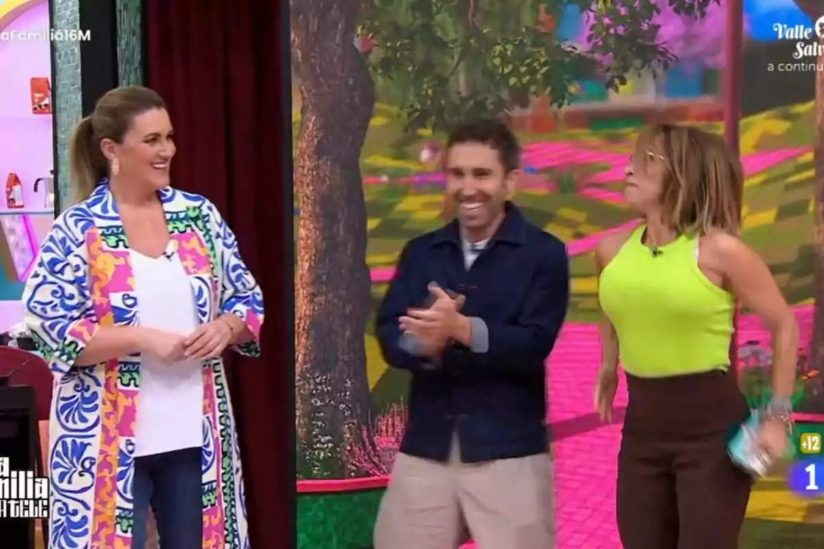 Carlota Corredera, Aitor Albizua y María Patiño sonríen y aplauden en un set de televisión colorido con un fondo de árboles y caminos en La Familia de la Tele. Carlota Corredera, Aitor Albizua y María Patiño sonríen y aplauden en un set de televisión colorido con un fondo de árboles y caminos en La Familia de la Tele.