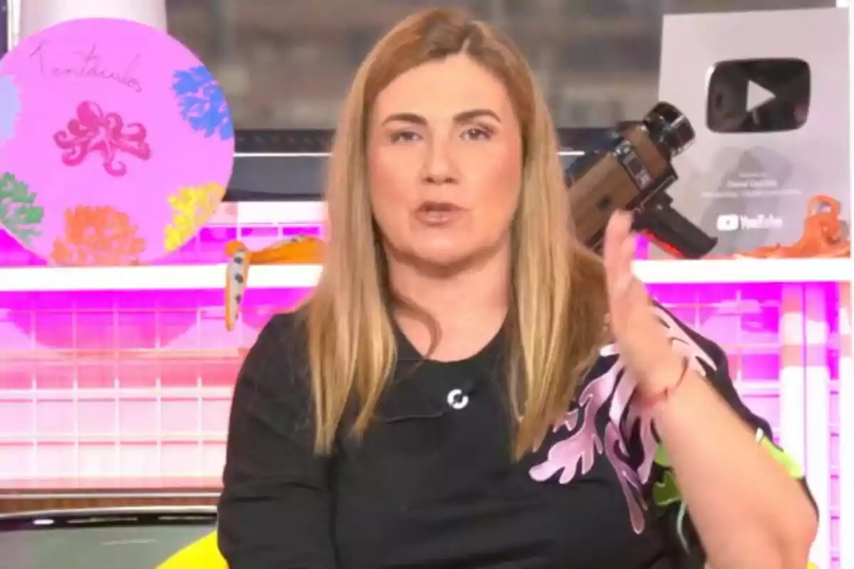 Carlota Corredera con cabello rubio lacio hablando frente a la cámara con una placa de YouTube y decoraciones coloridas al fondo en 'Tentáculos'