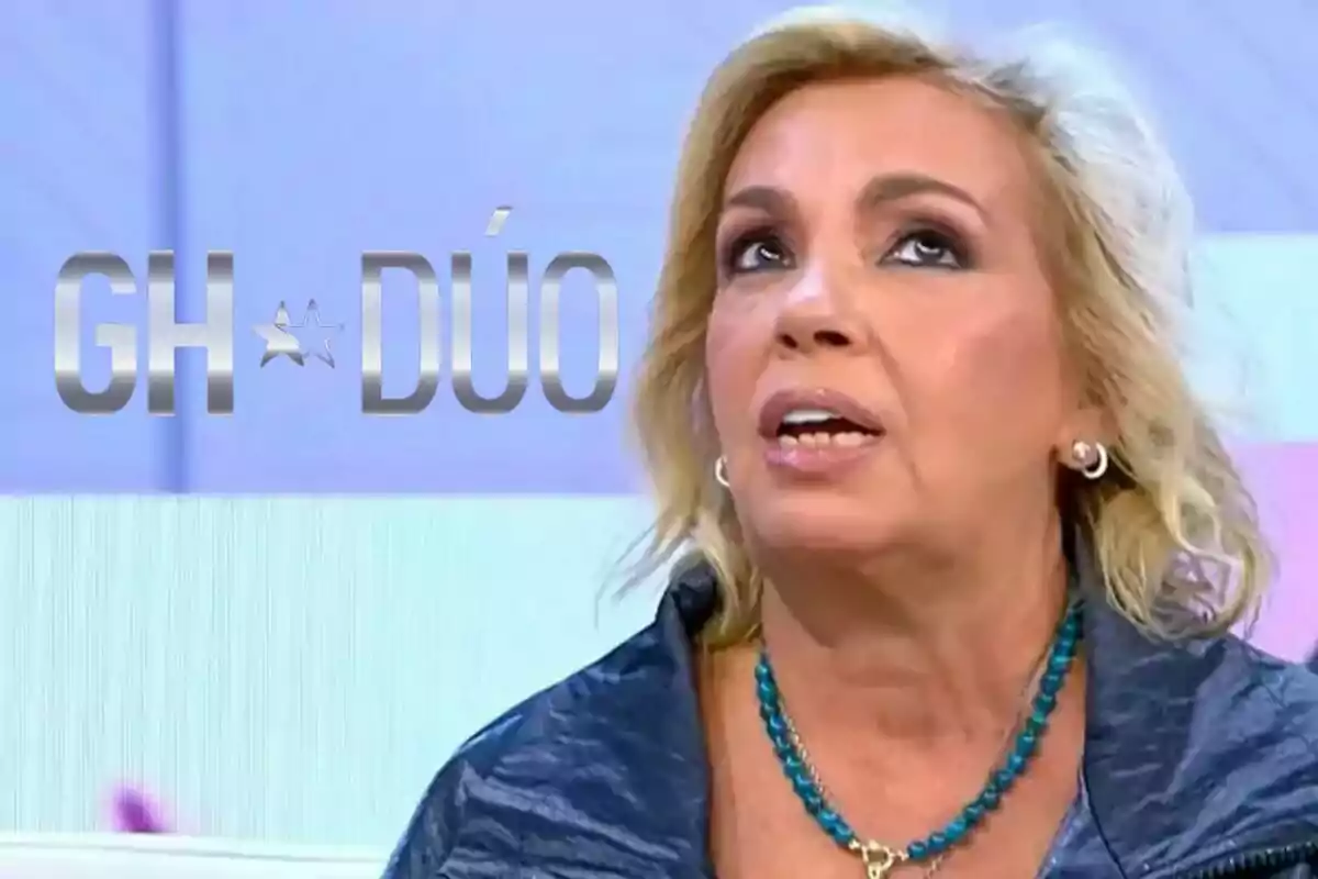 Carmen Borrego con cabello rubio y un collar azul aparece en un programa de televisión con el logo de "GH DÚO" en el fondo.