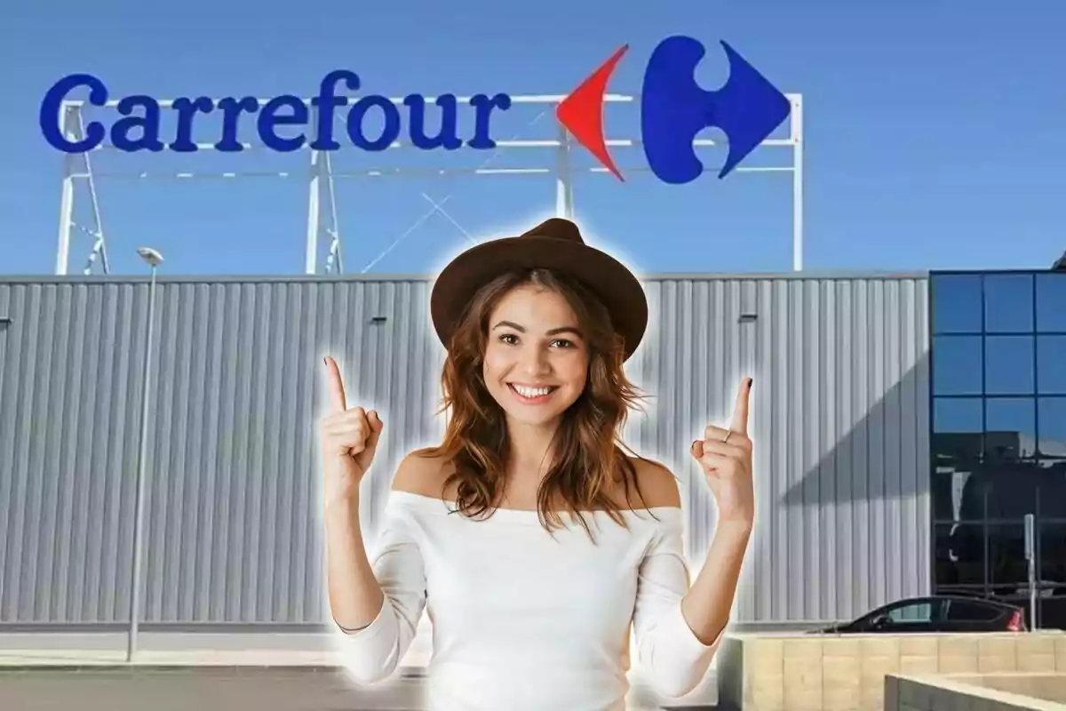 Mujer sonriente con sombrero y blusa blanca señalando hacia arriba frente a un edificio de Carrefour.