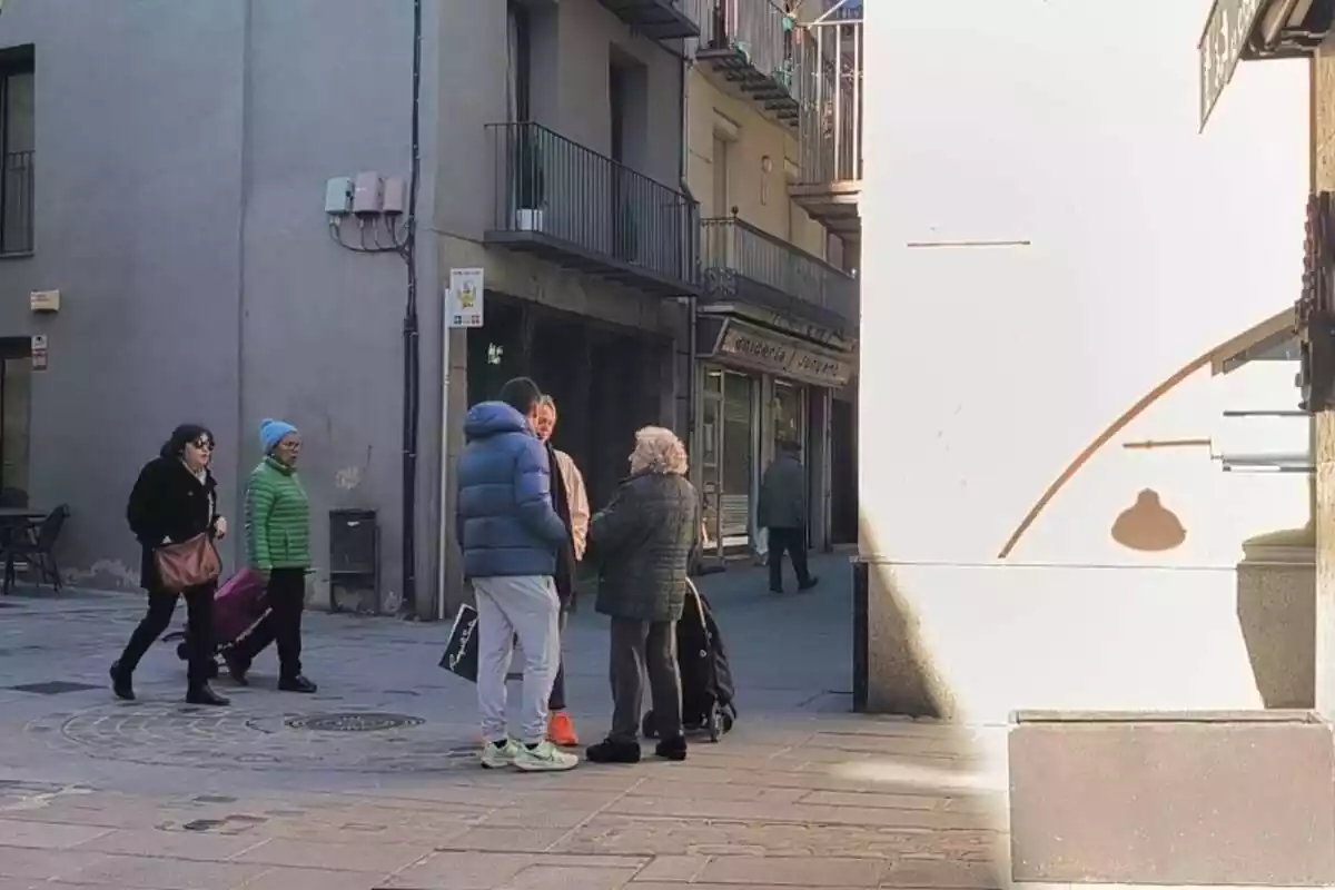 Imagen de dos calles de Ripoll con varios ciudadanos andando y hablando entre ellos Imagen de dos calles de Ripoll con varios ciudadanos andando y hablando entre ellos