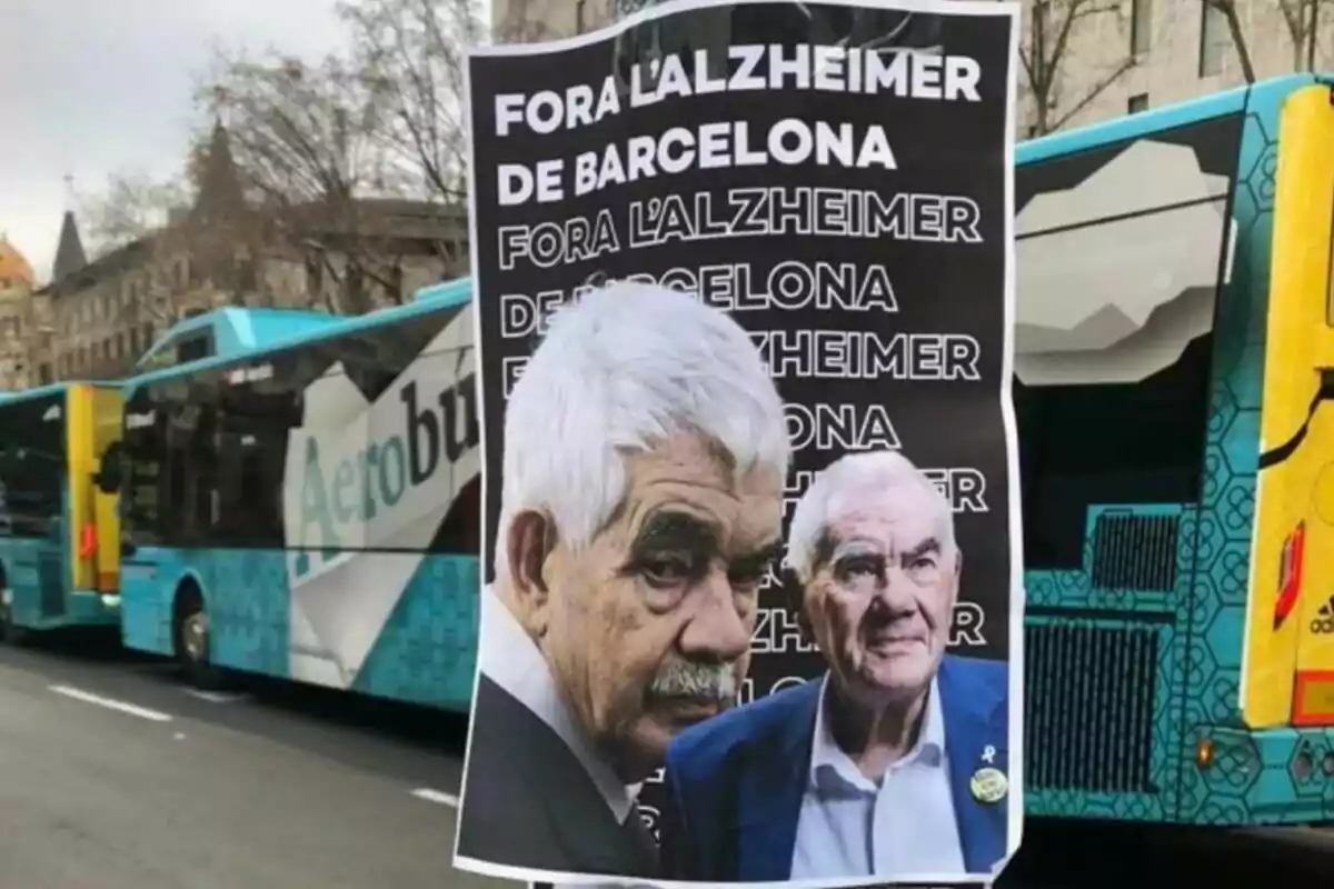 Cartel con el texto "Fora l'Alzheimer de Barcelona" repetido varias veces, con las imágenes de Pasqual y Ernes Maragall, pegado en un poste frente a varios autobuses en una calle de la ciudad.