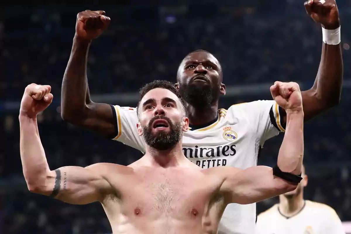 Dos jugadores de fútbol celebran con los puños en alto en un estadio.