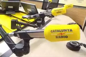 Imagen de una mesa de un estudio de grabación de Catalunya Ràdio, con 5 micros encima de la mesa con su característica espuma amarilla y el logo de la emisora
