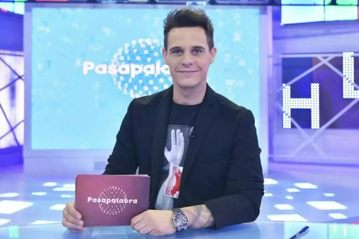 Christian Gálvez como presentador de televisión sostiene una tarjeta con el logo de Christian Gálvez como presentador de televisión sostiene una tarjeta con el logo de