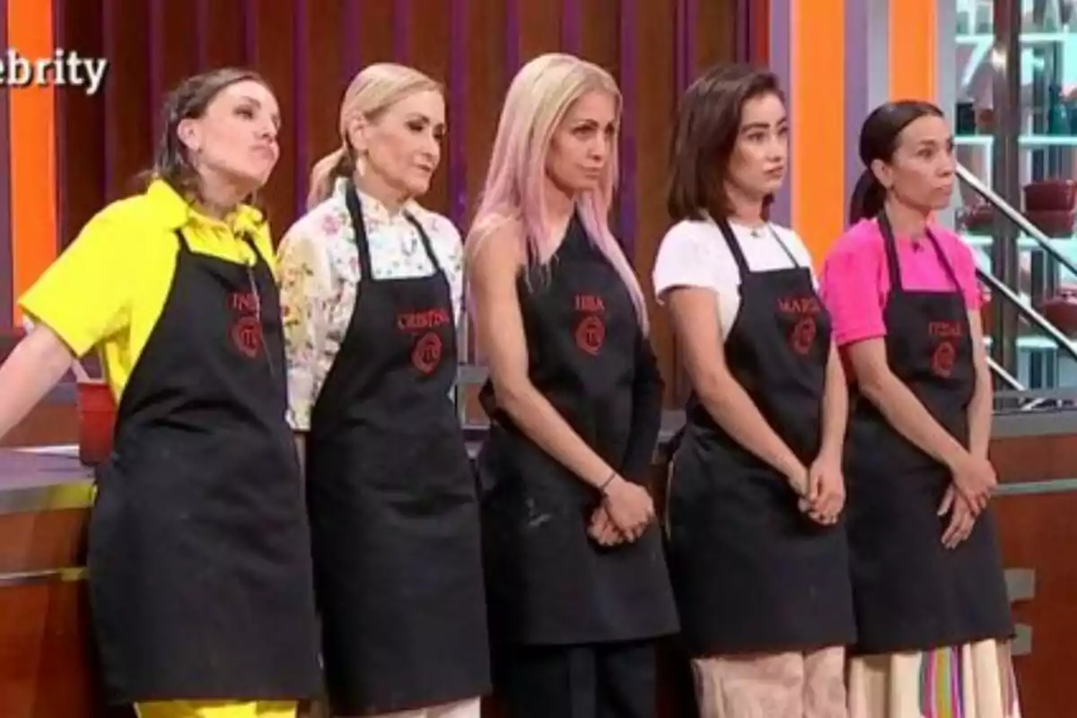 Inés Hernand, Cristina Cifuentes, Hiba Abouk, Marina Rivers e Itziar Miranda con delantales negros de MasterChef Celebrity están de pie en una cocina de televisión.