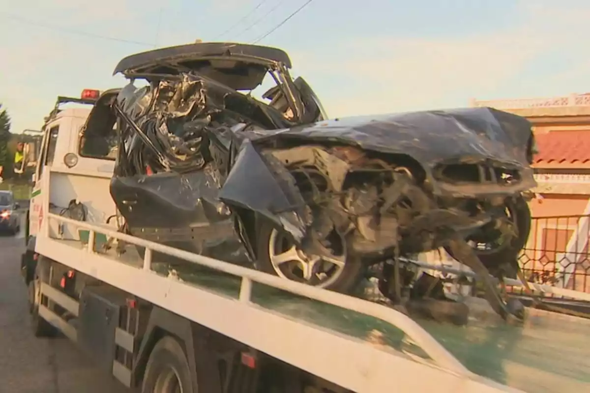 Un coche gravemente dañado es transportado por una grúa en una calle.