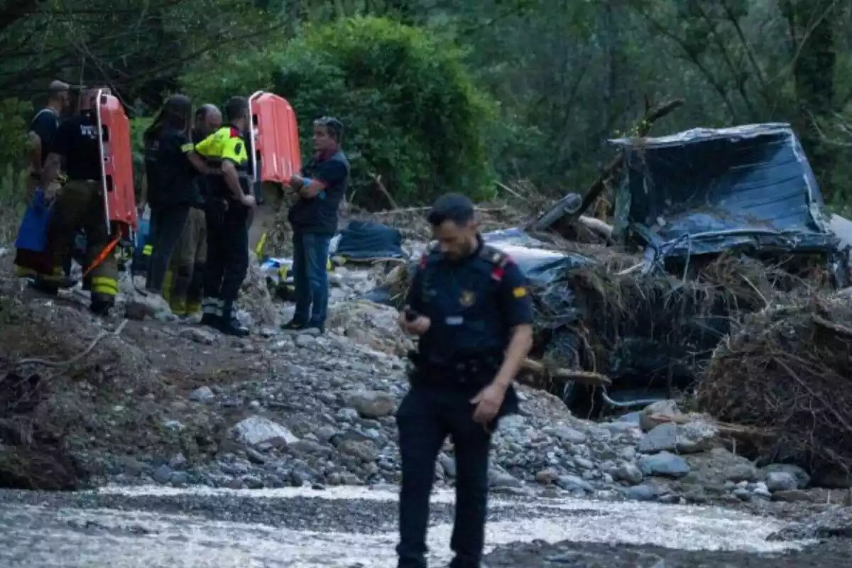 Parte del río con un coche destrozado junto a los Mossos d'Esquadra y los bomberos