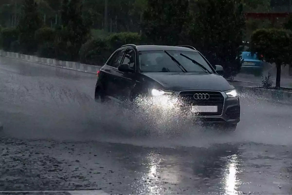 Un coche oscuro atravesando un charco de agua en medio de una tormenta