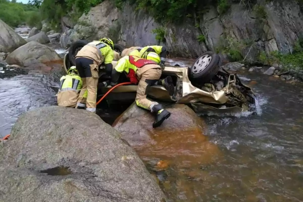 Bomberos rescatan a una persona de un automóvil volcado en un arroyo entre rocas.