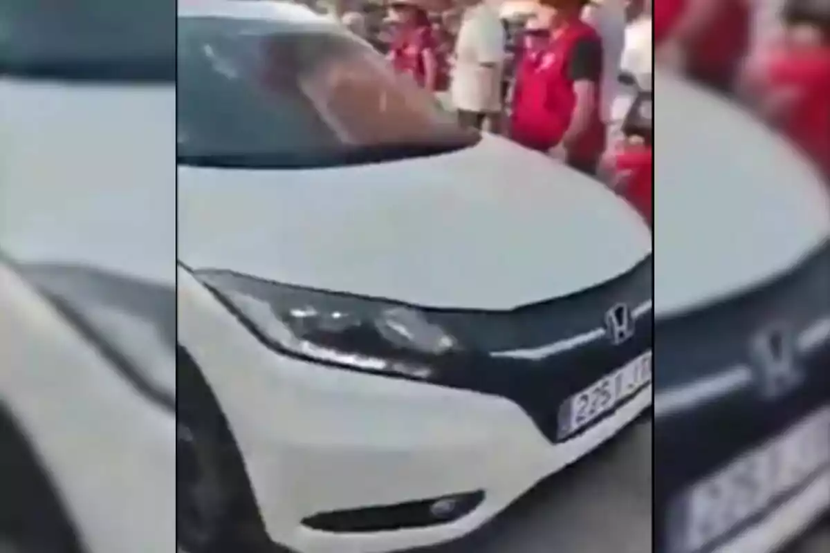 Un coche blanco Honda rodeado de personas con chalecos rojos.