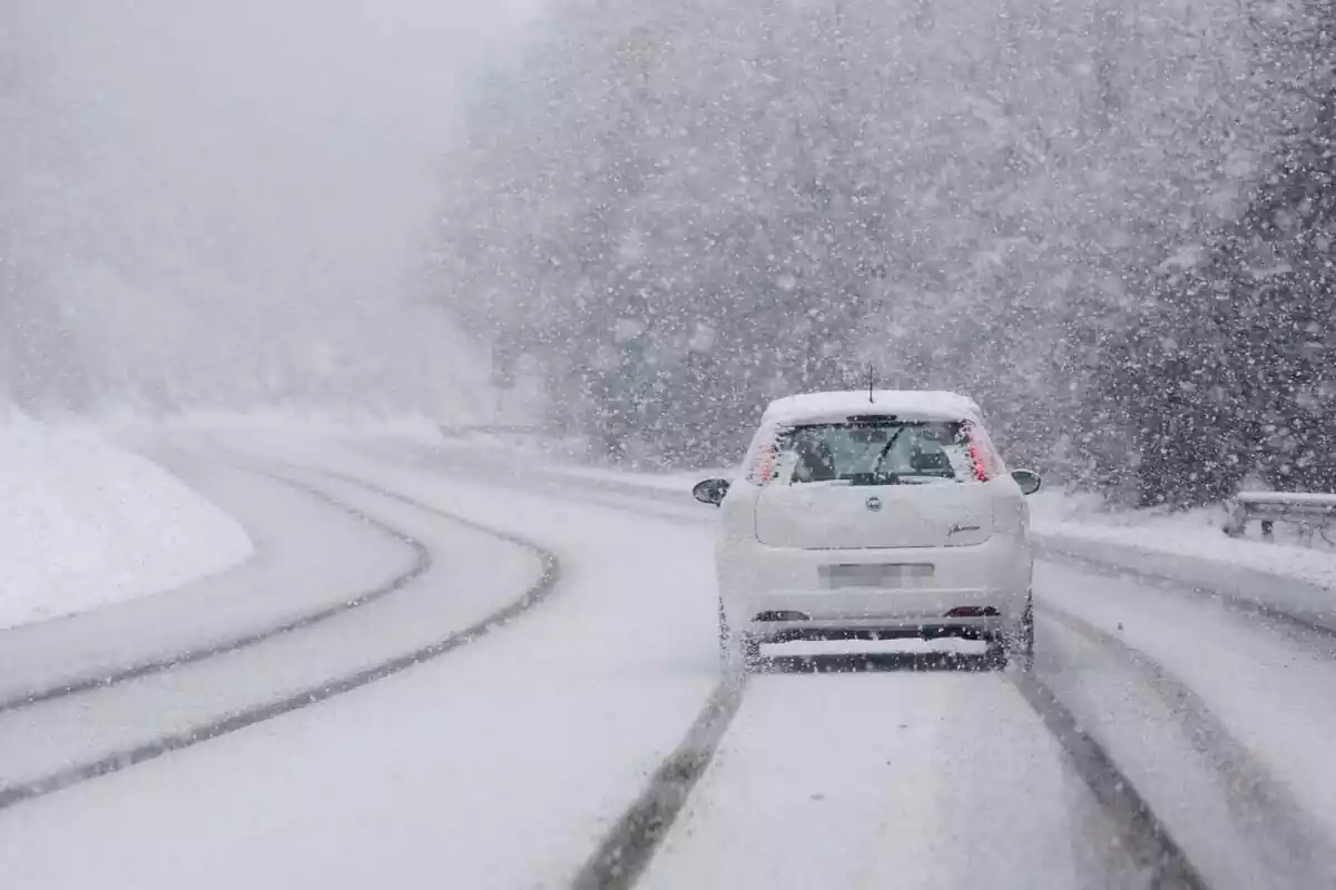 Un coche circulando en mitad de la nevada por una carretera bastante llena de nieve