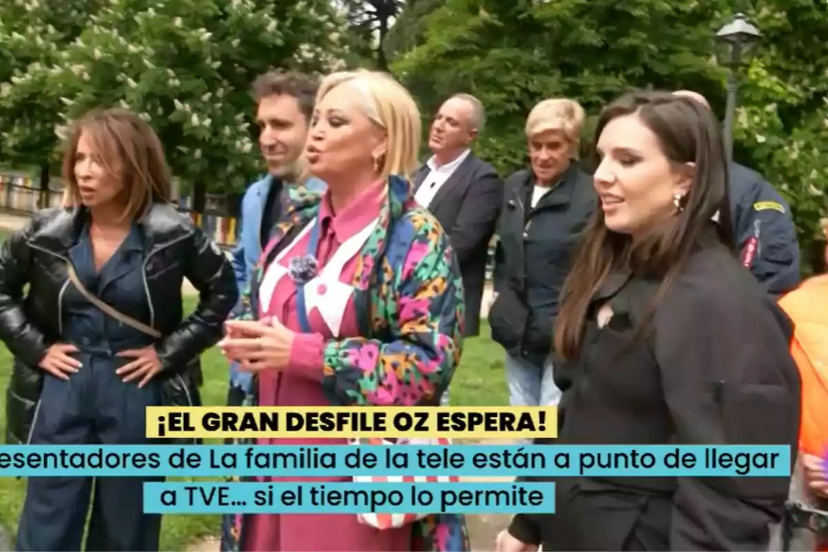 Un grupo de personas formado por Belén Esteban, María Patiño, Aitor Albizua, Inés Hernand, Victor Sandoval, Chelo García Cortés y Kiko Matamoros está reunido al aire libre, algunas de ellas conversan mientras otras observan, y hay un cartel que menciona un desfile en La Familia de la Tele.