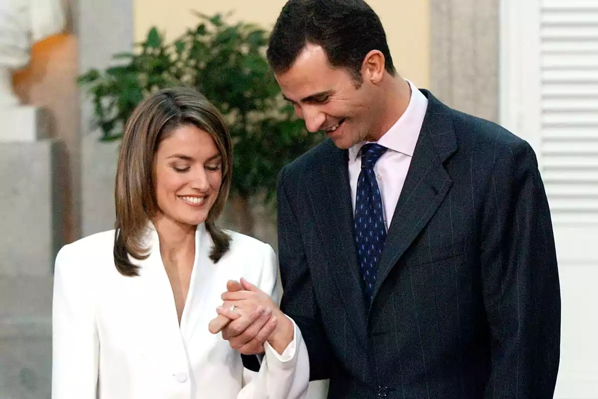 La reina Letizia y Felipe VI sonriente se mira mientras se toman de las manos en un entorno formal. La reina Letizia y Felipe VI sonriente se mira mientras se toman de las manos en un entorno formal.