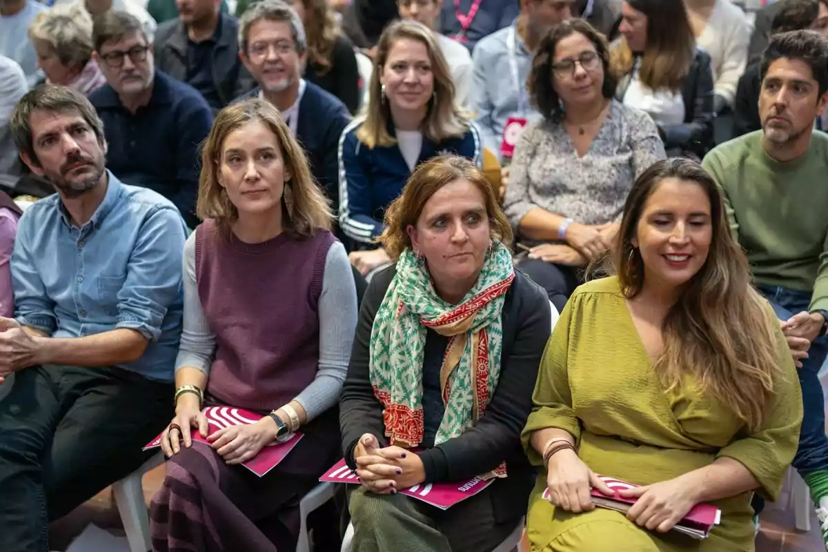 Un grupo de personas sentadas en un evento, algunas sosteniendo folletos.