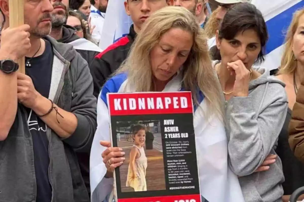 Una manifestante proisraelí cabizbaja con una bandera de Israel a la espalda y un cartel con una foto de una niña secuestradas por Hamás. A su lado, otros manifestantes