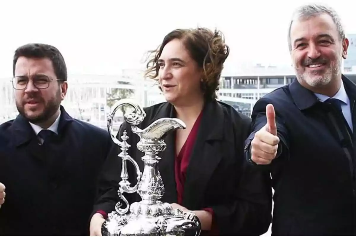 Tres personas posan juntas mientras una de ellas sostiene un trofeo plateado.