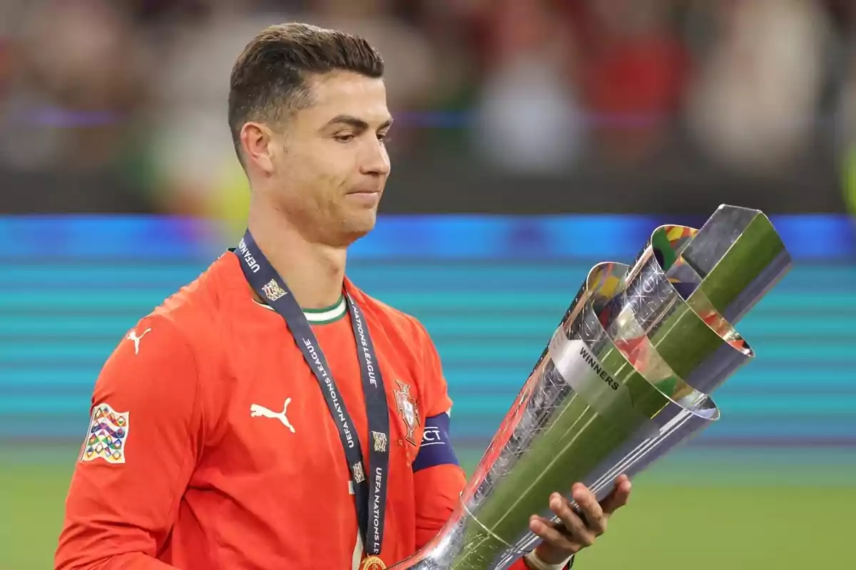 Futbolista con uniforme rojo sosteniendo un trofeo plateado en una ceremonia de premiación Futbolista con uniforme rojo sosteniendo un trofeo plateado en una ceremonia de premiación