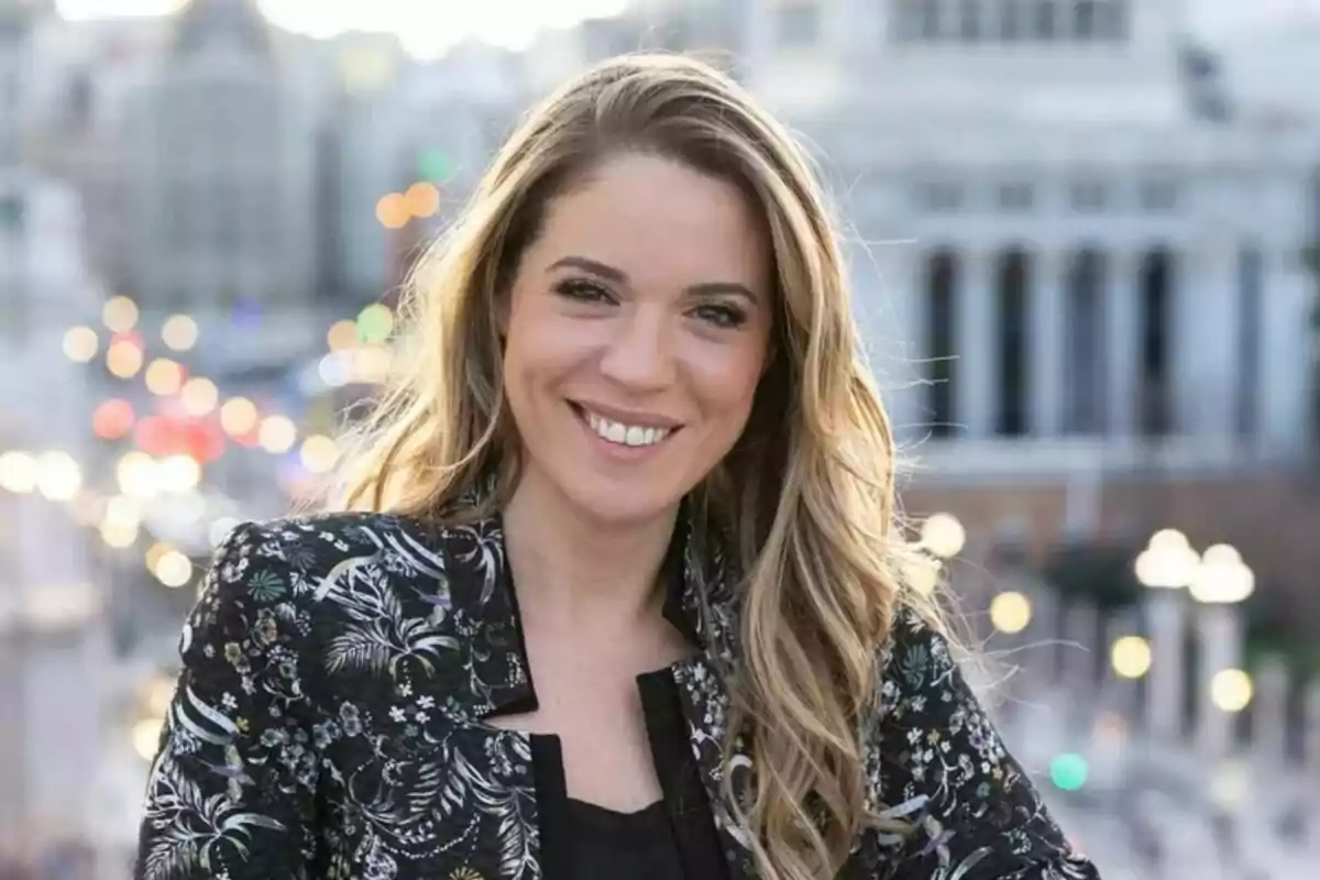Cristina Lasvignes joven de cabello rubio y largo sonriendo al aire libre con fondo urbano desenfocado y luces de la ciudad al atardecer Cristina Lasvignes joven de cabello rubio y largo sonriendo al aire libre con fondo urbano desenfocado y luces de la ciudad al atardecer