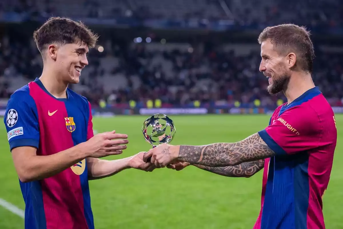 Dos futbolistas del Barcelona sonríen mientras uno le entrega un trofeo al otro en el campo de juego Dos futbolistas del Barcelona sonríen mientras uno le entrega un trofeo al otro en el campo de juego