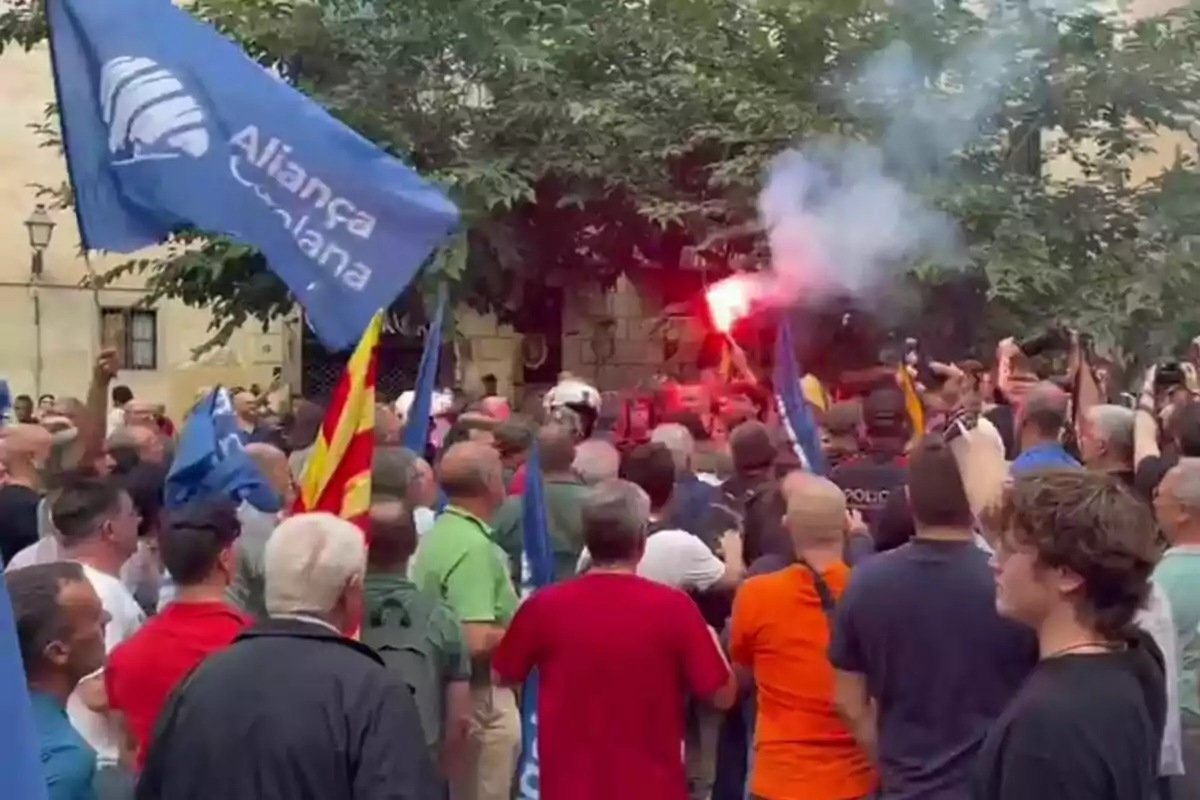 Una multitud de personas se ha reunido en una manifestación, algunas de ellas portando banderas y bengalas encendidas.