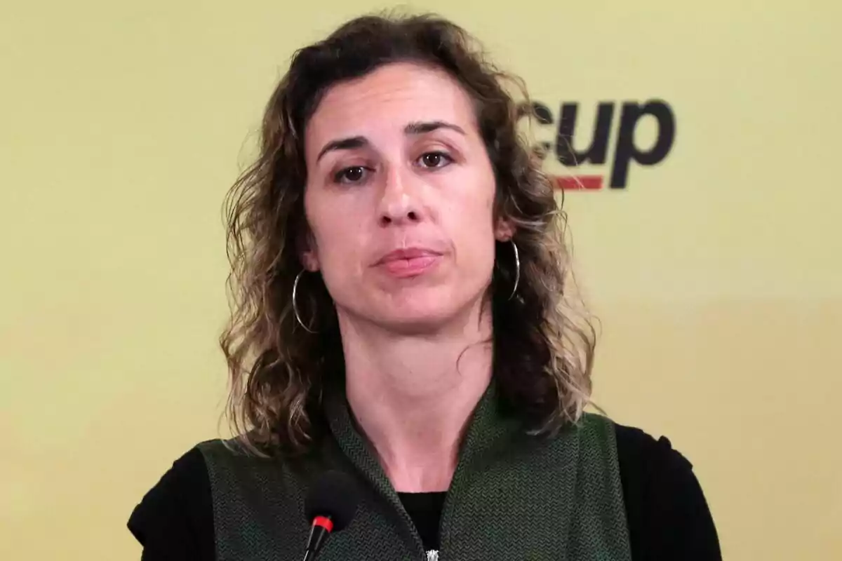 Laia Estrada hablando frente a un micrófono con un fondo amarillo y el logo de "cup" parcialmente visible.