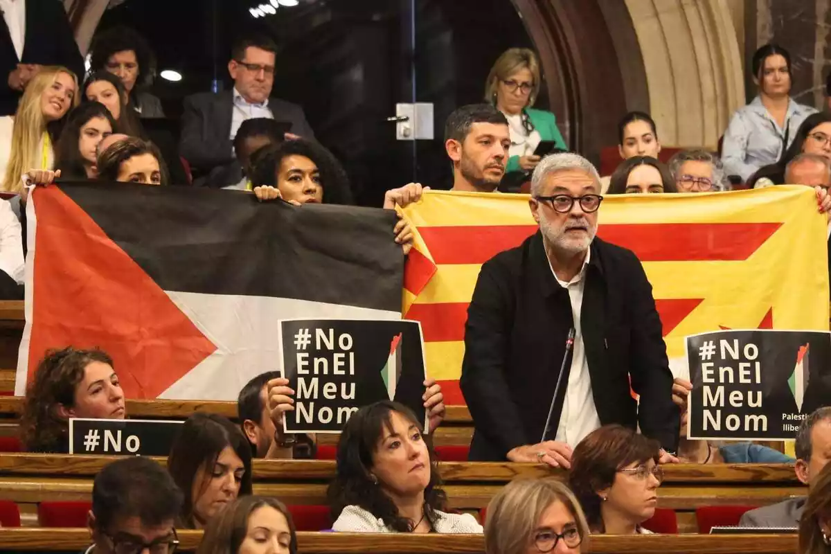 Carles Riera de la CUP interviniendo en el Parlament con otros diputados de la CUP por detrás mostrando una bandera estelada y otra de Palestina